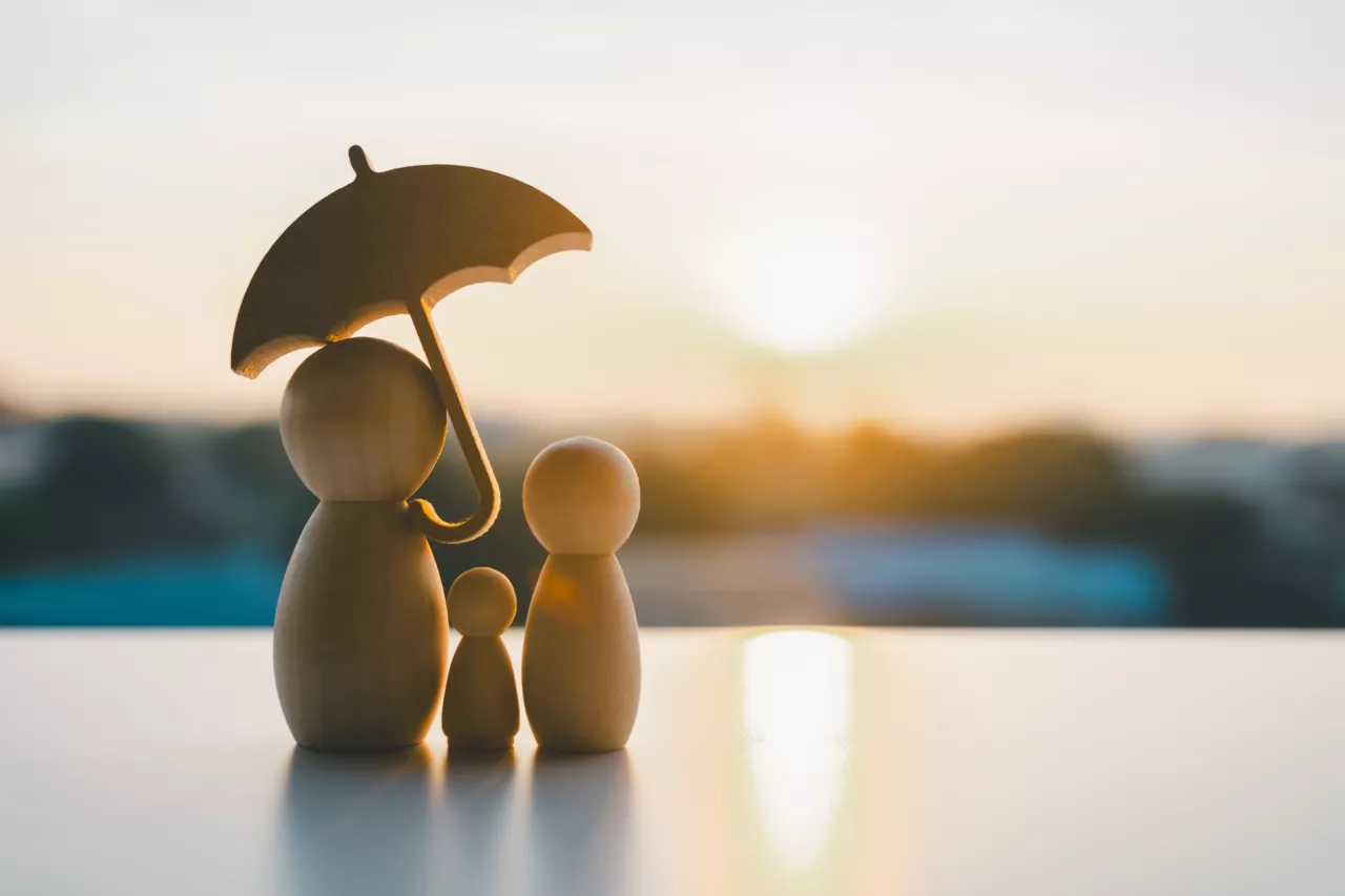 Schirm über Holzfiguren einer Familie bei Sonnenuntergang als Symbol für Schutz